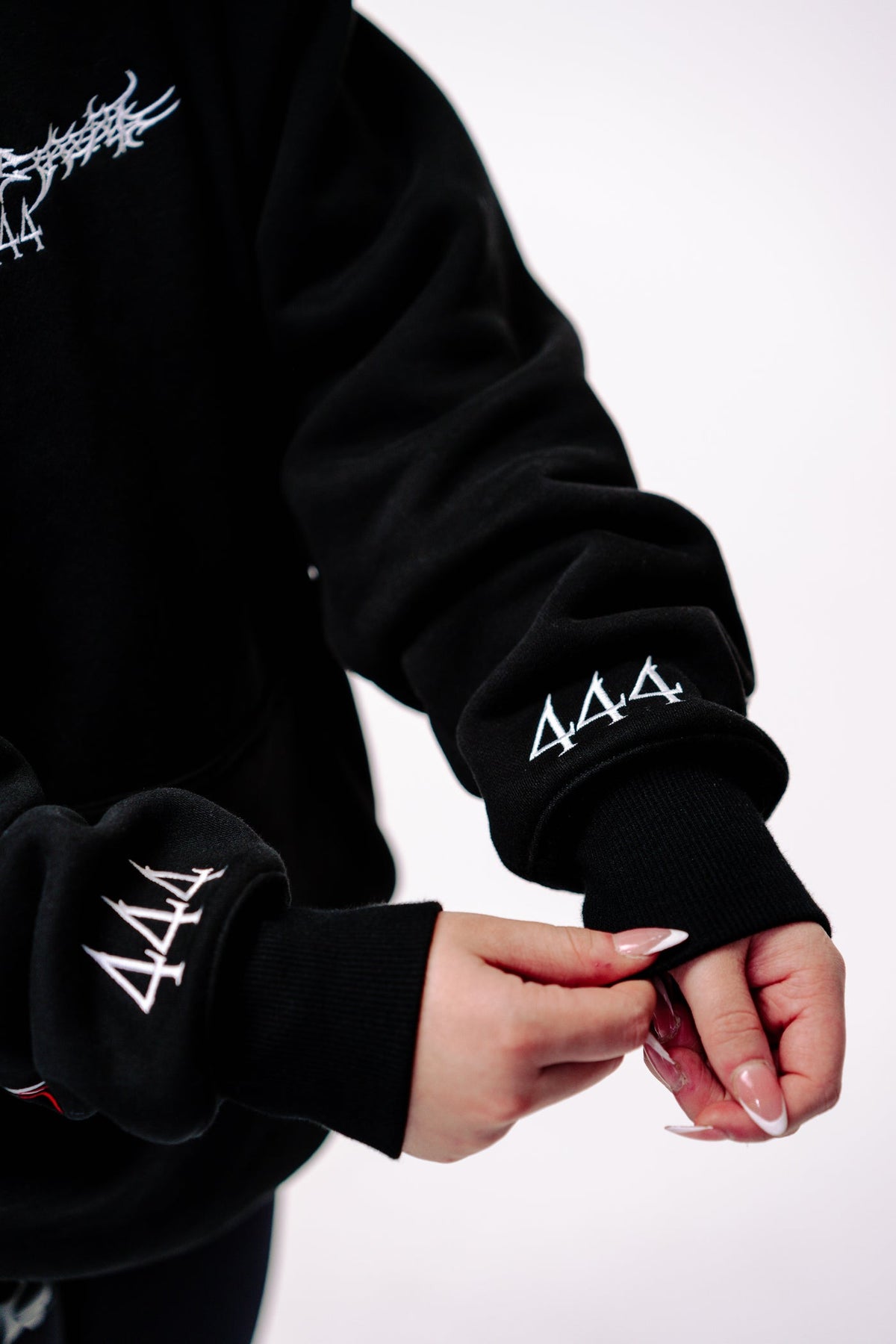 Detail of the Reflective Hoodie v2 cuffs, each carrying a white 444 mark above the ribbed hem, with the white chest print visible above.
