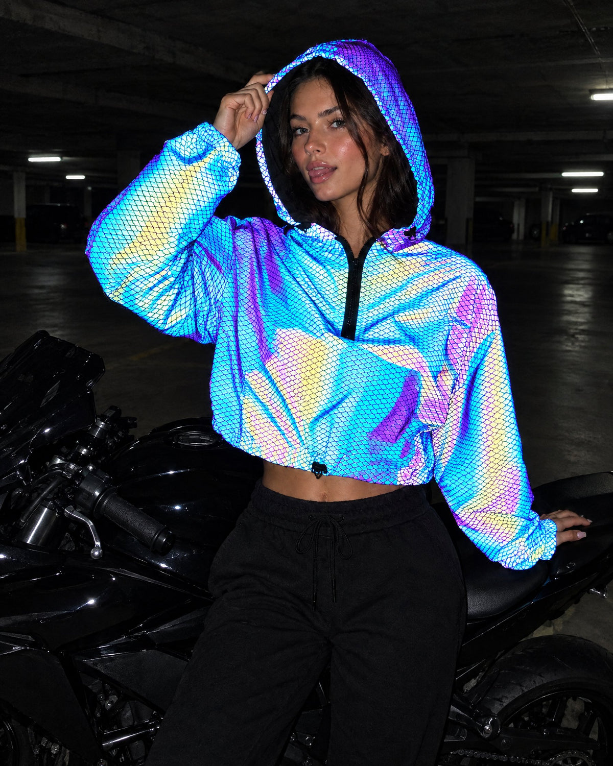 Scale reflective cropped jacket glowing with a fish-scale pattern under phone flash in a parking garage